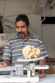 man selling dough in nixtamal mill. A pendulum scale is being used to weigh the dough.