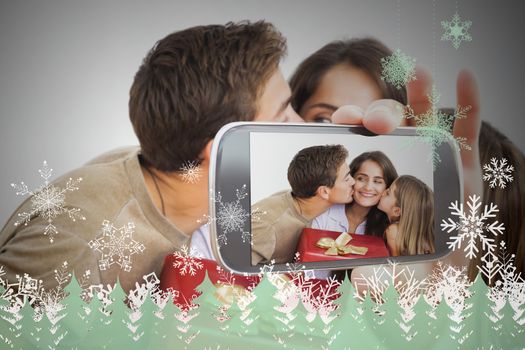 Hand holding smartphone showing photo against snowflakes and fir trees in green