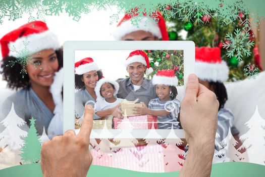 Hand holding tablet pc against snowflakes and fir tree in green