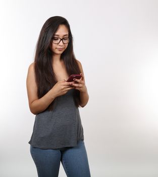 A pretty young girl wearing glasses is distracted; looking at her phone.