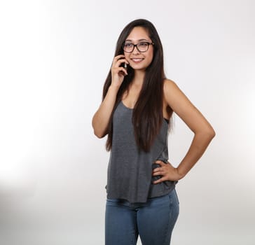 A young girl in jeans and glasses smiles as she hold her cell phone close to her ear.