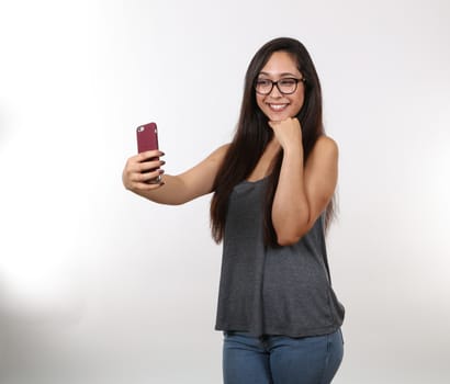 An attractive female wearing glasses in casual clothes takes a selfie on her phone.