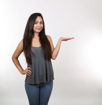 A pretty lady wearing jeans holds her hand out as she smiles.