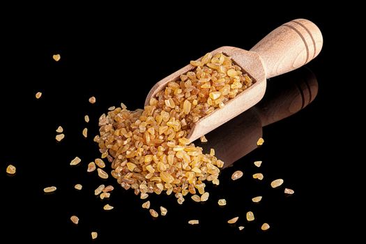 Dry bulgur in the scoop on black background