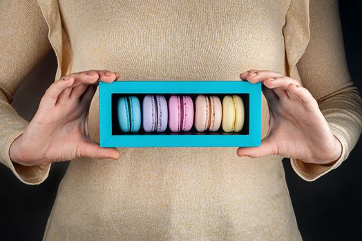 Beautiful female hands hold colorful macaroons in gift box