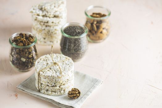 American puffed rice cakes. Healthy snacks with almonds, raisins, peanuts, pistachios in glass jars on light pink concrete surface. Copy space for you text.