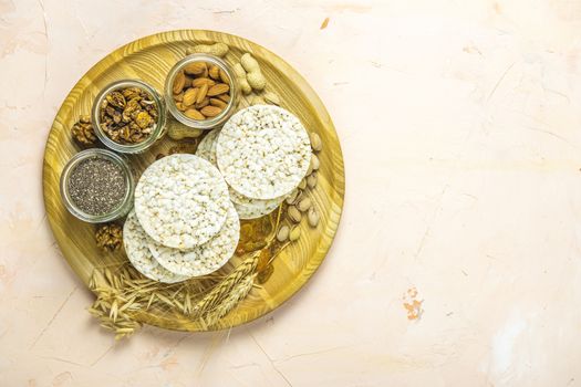 American puffed rice cakes. Healthy snacks with ears of wheat on round cutting wooden board on light pink concrete surface, top view, flat lay, copy space for you text	