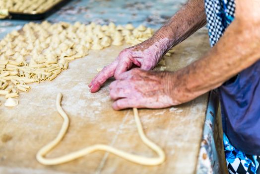 An old woman, while prepare by hands Orecchiette, typical italian pasta.