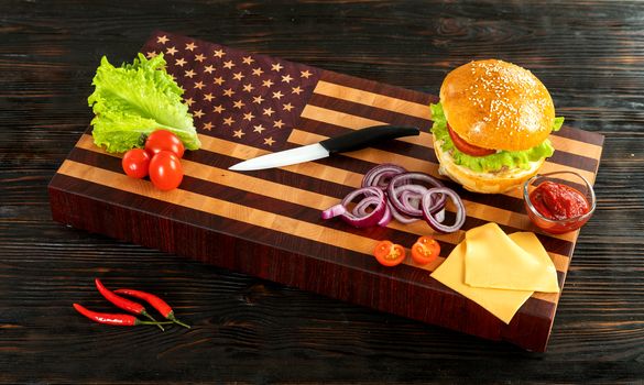 Burger next to vegetables and cheese on a wooden cutting board