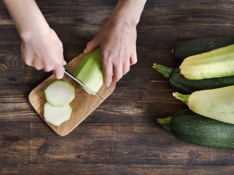 Zucchini harvest. Woman slices zucchini on wooden table. Farm organic zucchini harvesting