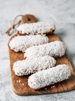 Homemade eclairs with coconut on wooden cutting board. Close up view of delicious healthy profitroles with shredded coconut. Copy space for text or design. Vertical.