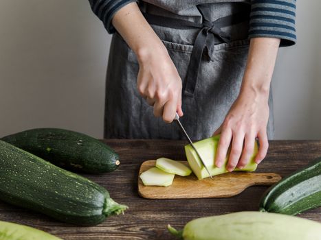 Zucchini harvest. Woman slices zucchini on wooden table. Farm organic zucchini harvesting