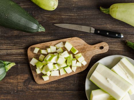 Zucchini harvest. Slices farm organic zucchini cubes for freezing on woodencutting board over brown wooden table. Zucchini harvesting concept.