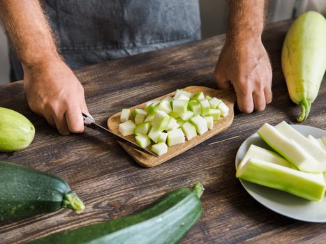 Zucchini harvest. Man slices zucchini cubes for freezing on wooden table. Farm organic zucchini harvesting