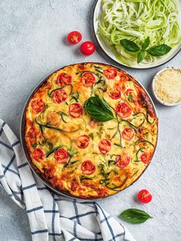 Zucchini pie and ingredients on gray background. Top view of delicious savory pie with zucchini, tomatoes, herbs and cheese. Idea and recipe for healthy baking and lot to harvest of zucchini. Vertical