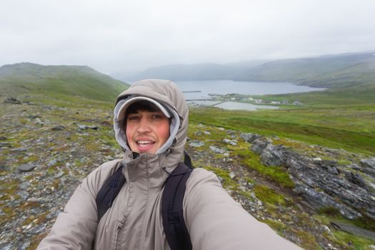 Tourist man making selfie on hill near Skarsvag (near Nordkapp). Landmark on Lofoten islands. Norway.