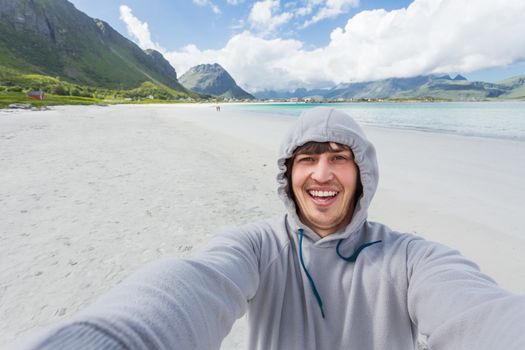 Tourist man making selfie on Rambergstranda beach on Lofoten islands. Beautiful sandy beach and azure water. Norway.