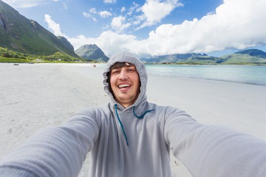 Tourist man making selfie on Rambergstranda beach on Lofoten islands. Beautiful sandy beach and azure water. Norway.