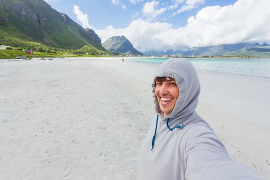 Tourist man making selfie on Rambergstranda beach on Lofoten islands. Beautiful sandy beach and azure water. Norway.