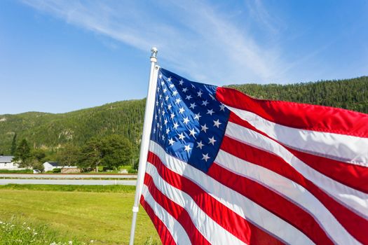 Flag of the United States of America (American flag or The Stars and Stripes, Old Glory, The Star-Spangled Banner) waving in the wind against summer forest landscape in sunny day.