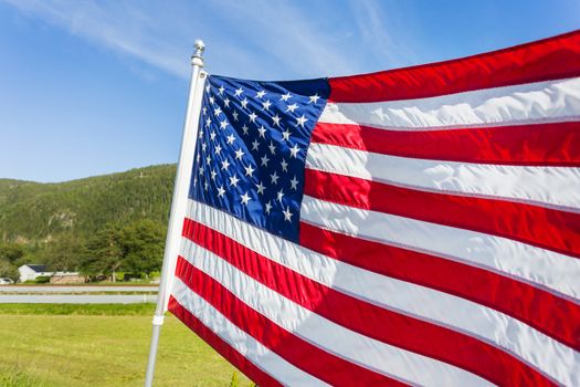 Flag of the United States of America (American flag or The Stars and Stripes, Old Glory, The Star-Spangled Banner) waving in the wind against summer forest landscape in sunny day.