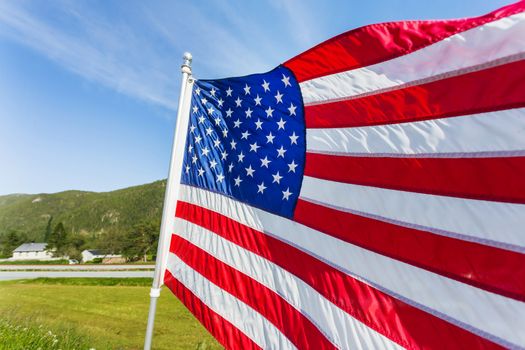 Flag of the United States of America (American flag or The Stars and Stripes, Old Glory, The Star-Spangled Banner) waving in the wind against summer forest landscape in sunny day.