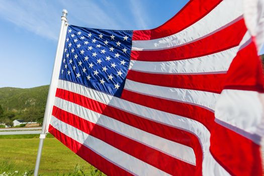 Flag of the United States of America (American flag or The Stars and Stripes, Old Glory, The Star-Spangled Banner) waving in the wind against summer forest landscape in sunny day.