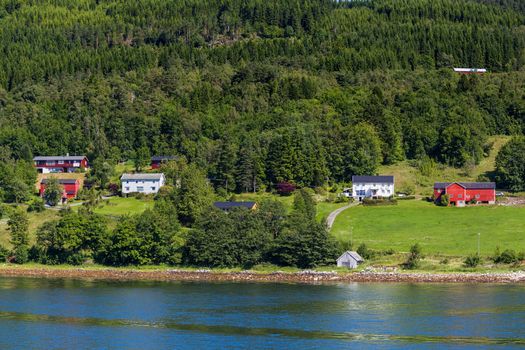 Typical scandinavian landscape with meadows and village. Houses with red walls and roofs. Norway.