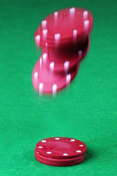 Some red casino chips falling onto a card table with motion blur