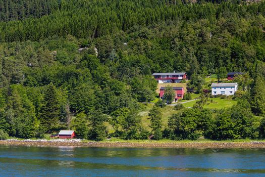 Typical scandinavian landscape with meadows and village. Houses with red walls and roofs. Norway.