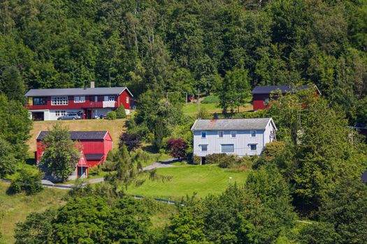 Typical scandinavian landscape with meadows and village. Houses with red walls and roofs. Norway.