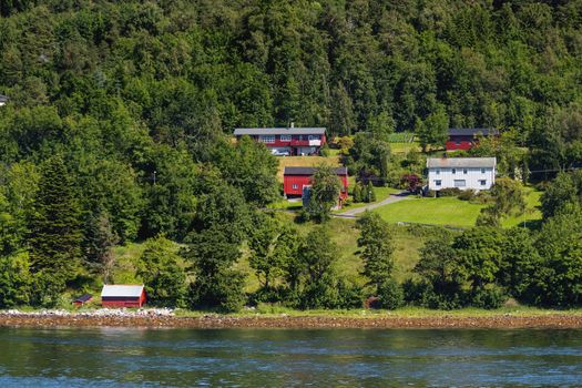 Typical scandinavian landscape with meadows and village. Houses with red walls and roofs, lawns. Norway.