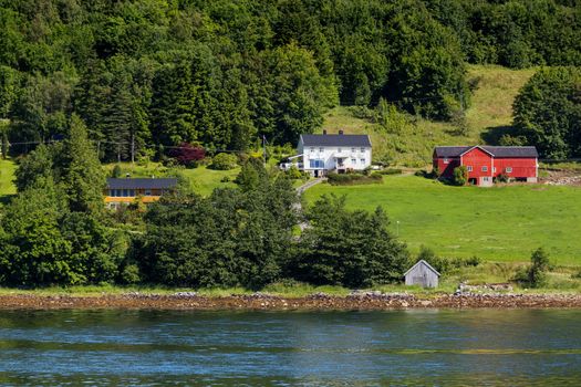 Typical scandinavian landscape with meadows and village. Houses with red walls and roofs. Norway.