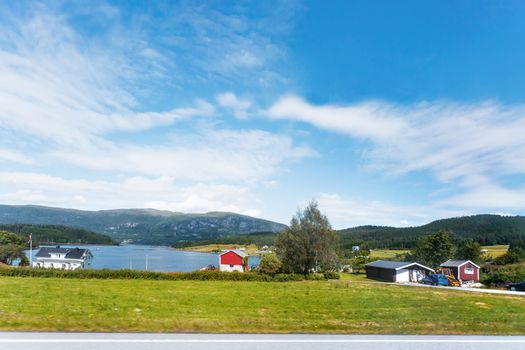 Typical scandinavian landscape with meadows, fjord and village. Houses with red walls and roofs on the bay. Norway.