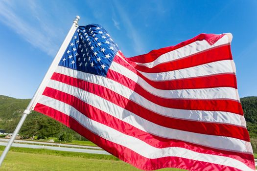 Flag of the United States of America (American flag or The Stars and Stripes, Old Glory, The Star-Spangled Banner) waving in the wind against summer forest landscape in sunny day.