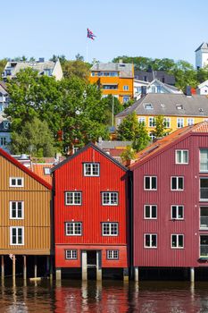 Famous wooden colored houses in Trondheim city, Norway. Colorful houses on stilts and flag of Norway in sunny day.