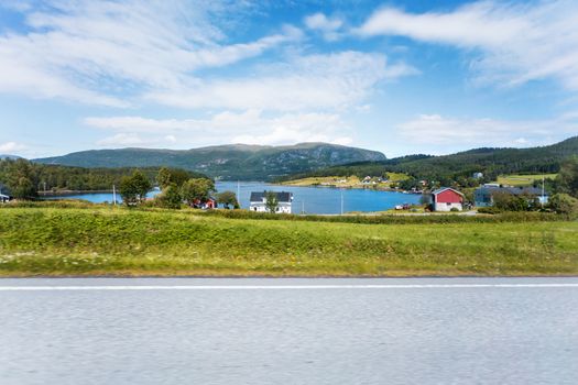 Typical scandinavian landscape with meadows, fjord and village. Houses with red walls and roofs on the bay. Norway.