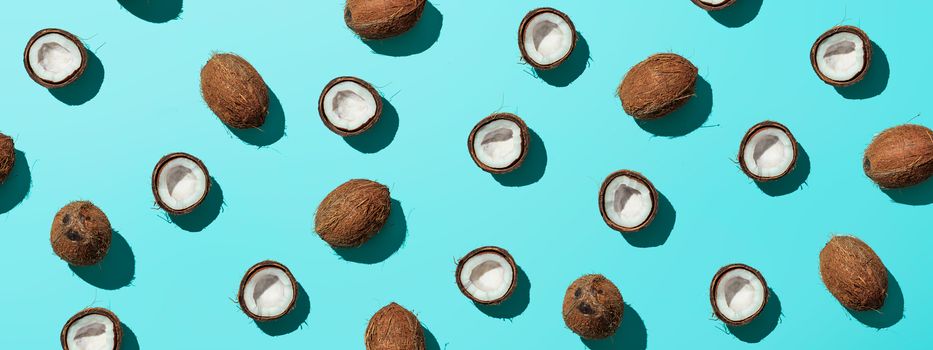 Creative layout of coconuts half on blue background. Tropical pattern, top view or flat lay. Hard light pop art minimal summer background. Horizontal banner