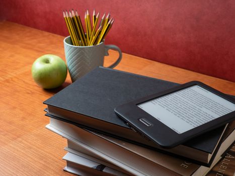 stacked classic books and an ebook with pens and apple