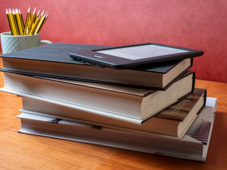 stacked classic books and an ebook with pens and apple