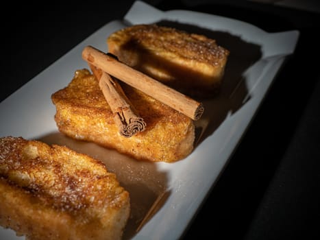 three french toast with cinnamon on white plate and dark background