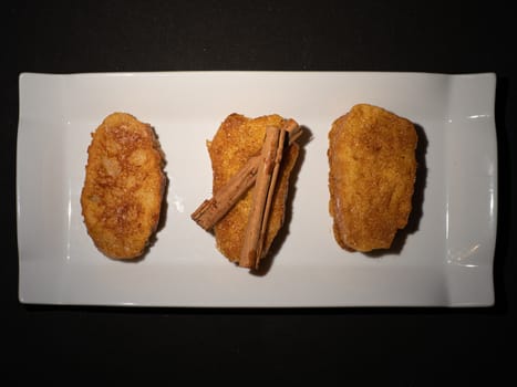 three french toast with cinnamon on white plate and dark background