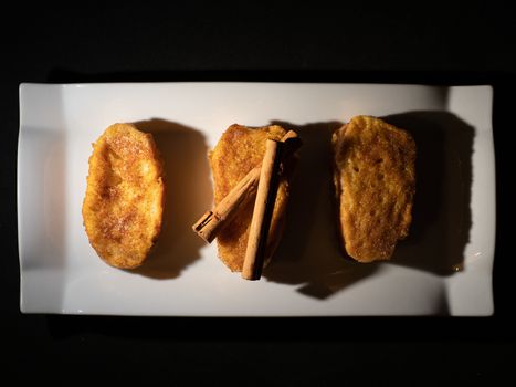 three french toast with cinnamon on white plate and dark background