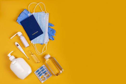 Coronavirus new lifestyle concept. Passports, sanitizer, thermometer, medical gloves, sanitizer gel, blue capsules pill in blister and medical mask on yellow colored background, flat lay