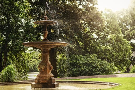 Archival and historical fountain in the park on a background of green trees on a sunny day (vintage effect)