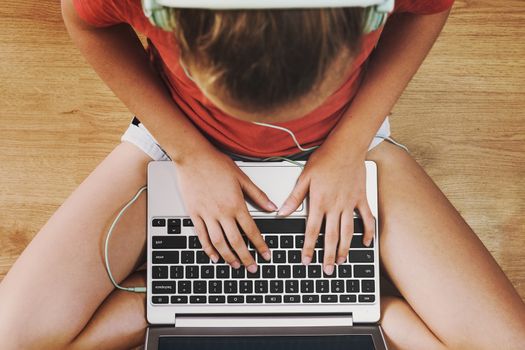 Top view of a girl sitting on the floor and communicating online on the internet on her laptop (vintage effect).