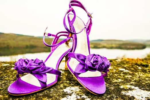 New purple velvet high heel shoes on a wall with lake behind UK