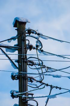 A convoluted mess of wires and cables clutter a wooden telephone pole and street lamp.