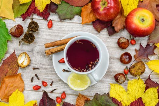A cup of warm tea with wild rose with spices and lemons and surrounded by autumn rustic decoration.