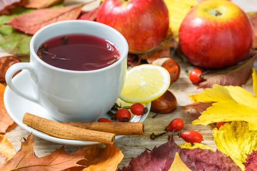 Concept of seasonal warm cup of tea with wild rose, spices, lemons and surrounded by autumn rustic decoration.